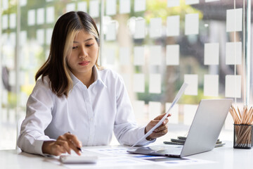 Woman working with laptop and reading business finance report document on office desk.