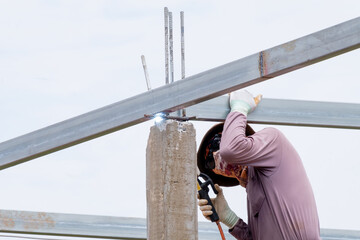 Construction worker men welding roof steel beams, man works with a welding machine and metal, House...