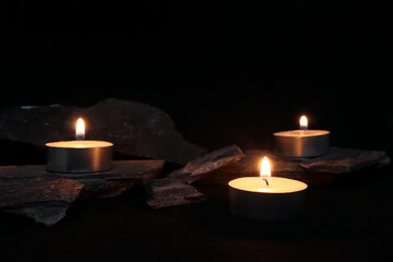 aromatic scented tealight candles are on black table with many stones and background of black wall...