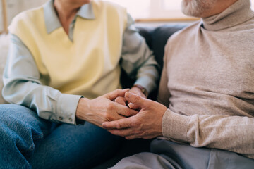 Crop couple holding hands and sitting on sofa