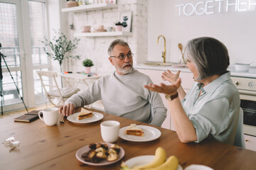 Happy elderly couple having breakfast and talking at home