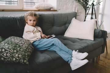 Cute little girl sitting on sofa and using smartphone