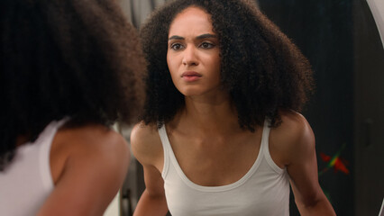 Worried young beautiful African American woman sad ethnic girl looking in mirror stressed about...