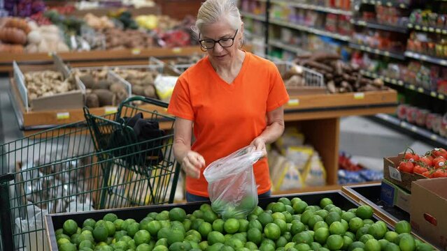 Slow motion portrait of smiling happy pretty mature woman selecting limes in a grocery store.