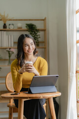 Asian freelance woman casually holding coffee mug working with tablet for internet surfing and blogging in cafe lifestyle business