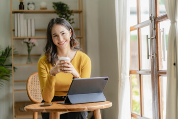 Asian freelance woman casually holding coffee mug working with tablet for internet surfing and blogging in cafe lifestyle business