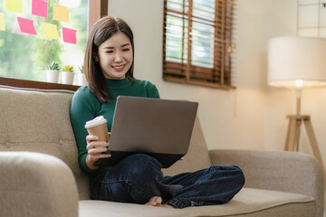 Happy asian girl holding tablet computer device using digital tablet technology sitting on sofa at...