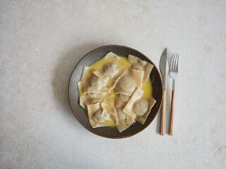 dish of homemade filled Italian pasta, ravioli with butter sauce, dark plate isolated on the table next to cutlery, knife and fork.