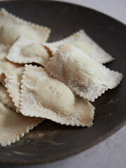 close up view of homemade uncooked freshly prepared Italian ravioli pasta in a dark plate