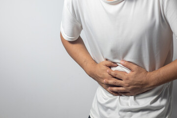 The man is holding his stomach with his hand against the white background, indicating that he has stomach pain. - obrazy, fototapety, plakaty