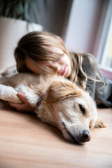 Low angle view of a toddler girl resting her head on her cute pet dog lying on the floor