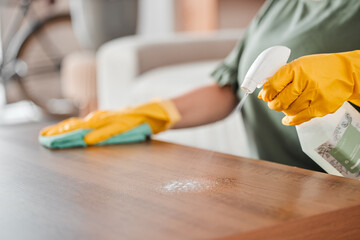 Hands, cleaning and spray on a wooden table for hygiene, disinfection or to sanitize a surface in a home. Gloves, bacteria and product with a woman cleaner in the living room for housework or chores