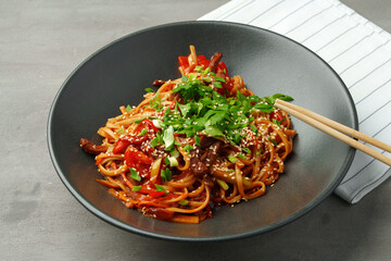 Stir fry noodles with vegetables and beef in black bowl on table