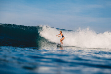 Surfer woman riding on ocean wave on surfboard. Woman during surfing with morning light