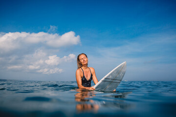 Surfer woman sitting on surfboard and wait waves. Woman with surfboard in ocean