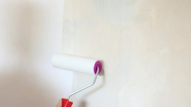 female hand applies primer with paint roller to wall