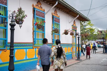 Fotobehang Couple walking at narrow street of Guatape with the famous colorful painted facades of the buildings.Selective focus, blurred background. © Elena Berd