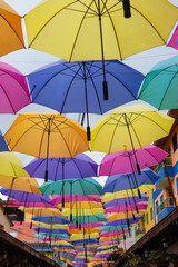 Obraz na płótnie Canvas Many bright colorful hanging umbrellas over a small cobblestone pedestrian street in Guatape Colombia - small tourist town near Medellin. Selective focus.