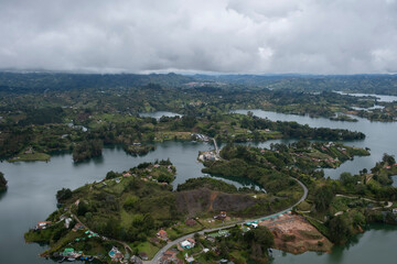 Fototapeta premium Aerial panoramic view of the hydroelectric reservoir, lakes, mountains and many small islands of Guatape covered with low clouds and fog on a rainy day with low visibility, near Medellin, Colombia.