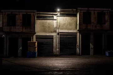  Old abandoned factory at night with a dirty front slightly illuminated by a light. © Anissa