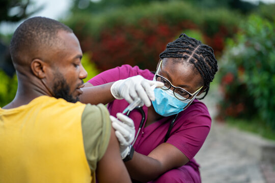 image of young african nurse in face mask, injecting young black guy outside- home care service in africa
