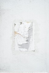 The remains of a white poster on a white wall, part of which has been torn off.