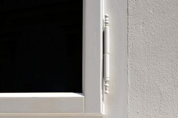 white painted wood window frame in stucco exterior wall. frontal elevation view. old style steel hinge. dark window glass. classic architecture. stippled stucco texture. construction and architecture.