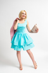 A woman in a blue elegant dress holds a pink coat and handbag in her hands