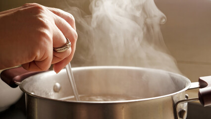 Female hand stirring boiling soup in pot. Healthy nutrition, cooking at home, hot steam.