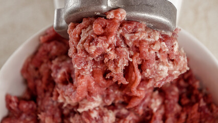 Closeup of minced meat coming out of electric grinder and falling in bowl. Cooking at home, kitchen...