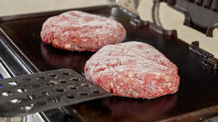 Closeup of hand putting frozen hamburger beef patties on hot grill. Cooking at home, kitchen appliance, healthy nutrition, hamburger ingredients.
