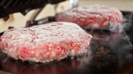 Closeup of cooking burgers on electric grill and closing the lid. Cooking at home, kitchen appliance, healthy nutrition, hamburger ingredients.