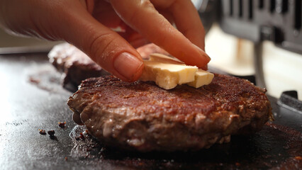 Closeup of hand putting butter on roasting beef burger patties on grill. Cooking at home, kitchen appliance, healthy nutrition, hamburger ingredients.