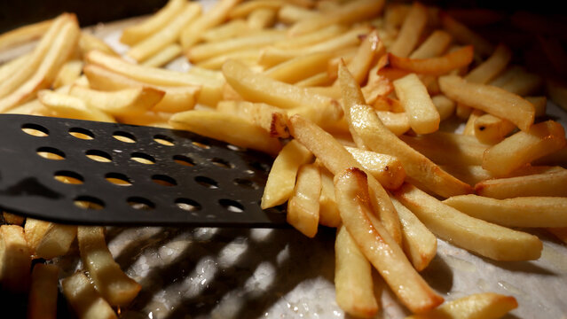 Closeup of stirring baking french fries in oven with spatula. Fast food, healthy nutrition, cooking in oven.