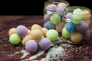 Colored round candy balls sprinkled with sugar a glass jar and on a wooden table.