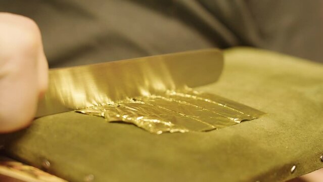 The artist cuts gold leaf into pieces to apply to the oil painting