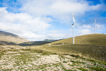 Fototapeta na wymiar Industry conceptual photo for a clean environment. A wind farm with wind turbines among the great mountains, the clouds, the meadows and the grazing animals. Peace and quiet against pollution 