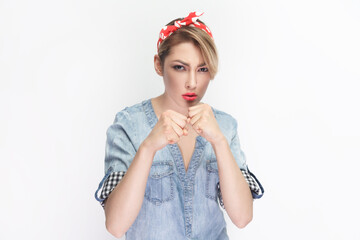 Obraz na płótnie Canvas Portrait of angry irritated blonde woman wearing blue denim shirt and red headband standing with clenched fists, fighting with somebody. Indoor studio shot isolated on gray background.