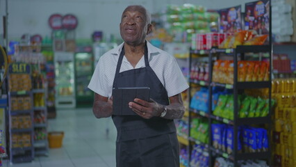 One senior black employee of supermarket holding tablet device and checking inventory. Job occupation concept using modern technology