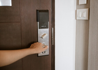 Woman's hand holding the door handle for closing, opening wooden door in bedroom with keyless entry card, smart lock system in a hotel