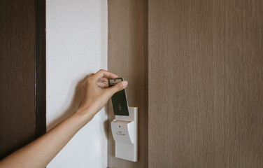 Female hand insert key card in holder on hotel room wall for opening main switch lock for enable...
