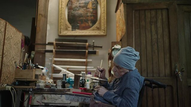 Elderly male master works in his workshop restoring japanese deba knife sheath