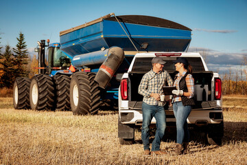 Farm couple uses tablet to monitor fall canola harvest while taking a coffee break, Alberta, Canada
