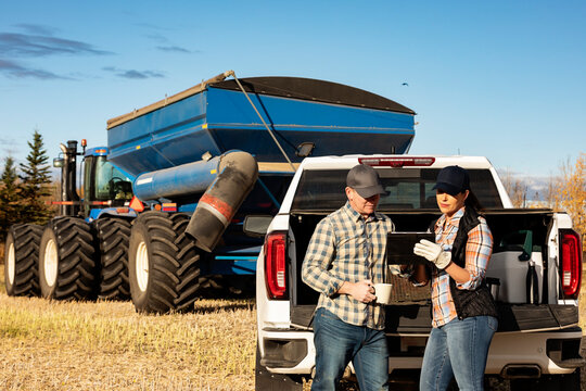 Farm couple uses tablet to monitor fall canola harvest while taking a coffee break, Alberta, Canada