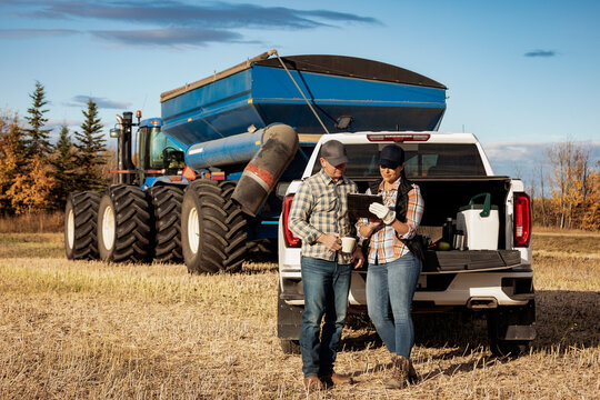 Farm couple uses tablet to monitor fall canola harvest while taking a coffee break, Alberta, Canada