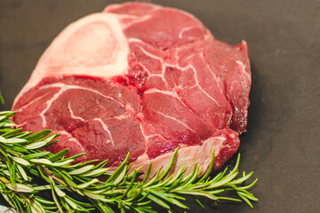 Fresh piece of meat large beef steak on the bone ossobuco with a sprig of rosemary on a black background.