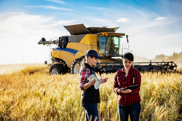 Woman farmer teaching apprentice advanced farming technologies during grain harvest, Alberta, Canada