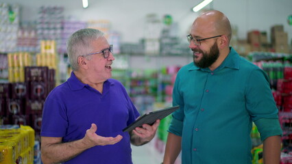 Senior manager of grocery store speaking with staff while looking at tablet device. Two men...