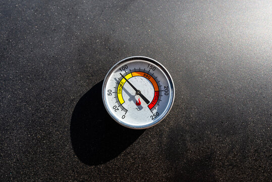 A round thermometer showing 90 degrees Celsius placed on a charcoal grill.