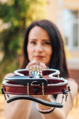 A woman artist with dark hair in a dress holds a wooden concert electric violin in her hands